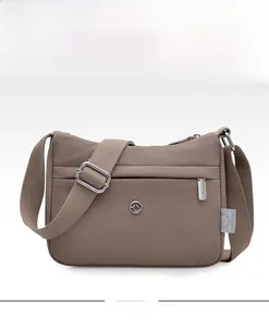Close-up of khaki nylon shoulder bag showing front zipper pocket and metal logo detail