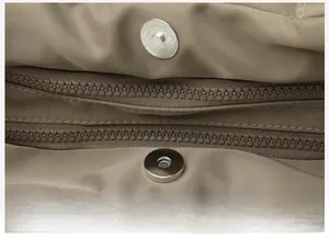 Detailed macro view of magnetic snap closures and dual metal zippers on nylon handbag