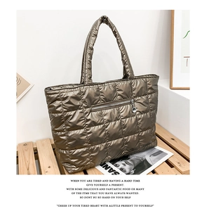 Detail of a large metallic bronze quilted tote bag with front zipper and metal charm
