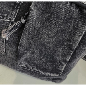 Macro detail of washed black denim fabric with white contrast stitching and a knotted zipper