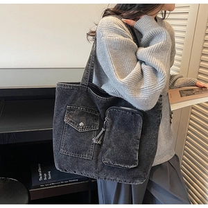 Detail of dark denim tote bag featuring fringe charm and multi-pocket front design
