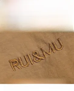 Detailed macro view of the RUI&MU logo embroidery on brown high-density nylon fabric
