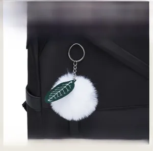 Close-up of fluffy white faux fur pom-pom charm with green leaf on a black backpack