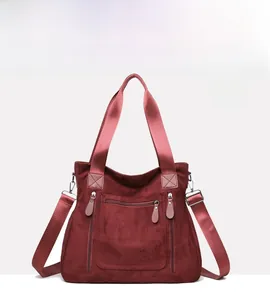 Detail of burgundy suede tote bag featuring silver zippers and adjustable shoulder strap