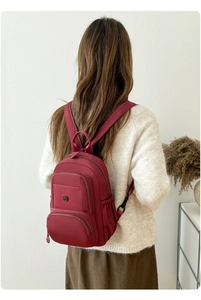 Detailed back view of a burgundy nylon backpack worn over a white knit sweater