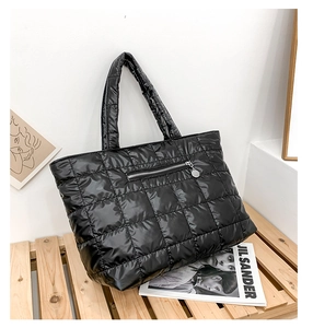 Close-up of a black quilted tote bag featuring a horizontal front zipper and padded handles