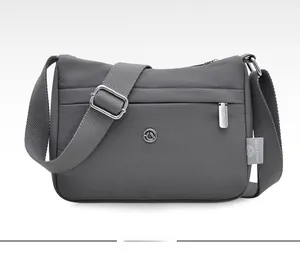 Front view of grey nylon crossbody bag with multi-layer zippers and adjustable strap