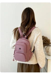 Close-up of a dusty pink waterproof nylon travel backpack worn by a model in a warm setting