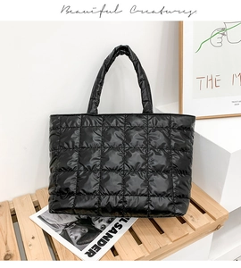 Close-up of a black quilted puffer tote bag with square stitching on a wooden bench