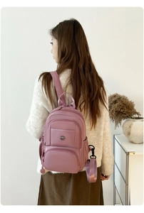 Dusty pink nylon travel backpack with multiple compartments shown on a female model
