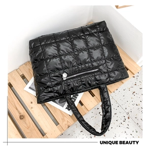 Detail of a black quilted tote bag featuring a front silver zipper and puffy nylon fabric