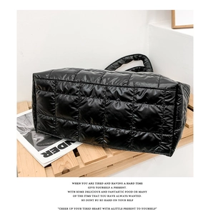 Detail of black glossy quilted tote bag featuring padded nylon texture on wooden stand