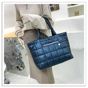 Detail of navy quilted puffer tote bag featuring front zip pocket and sleek nylon texture