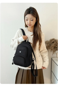 Detail of a minimalist black nylon backpack featuring a front zipper pocket and round logo