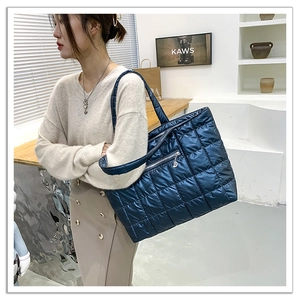 Detail of dark blue quilted tote bag featuring a front zipper pocket and glossy finish