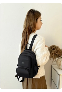 Detailed view of black nylon mini backpack with multiple zipper pockets on a female model