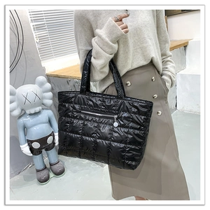 Close-up of black quilted puffer tote bag with square stitching and front zipper pocket