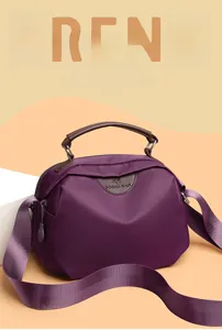 Detail of deep purple nylon crossbody bag featuring brown leather handle and brand tag