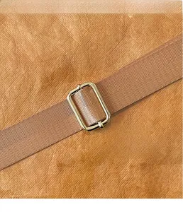 Detail of golden metal buckle with brown woven shoulder strap on lychee leather tote bag
