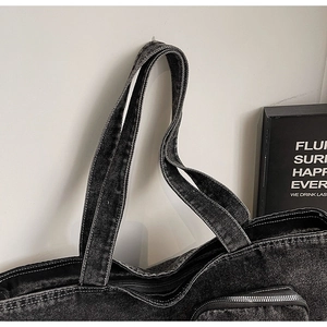 Detail of black washed denim tote bag showing metal zipper and sturdy dual handles