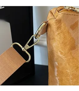 Detailed view of high-gloss gold metal D-ring and lobster clasp on caramel tote bag