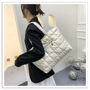 Detail of silver quilted tote bag showing metallic texture and zipper pocket on model