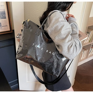 Detail of glossy black tote bag featuring bold white TOTE BAG text and wide strap