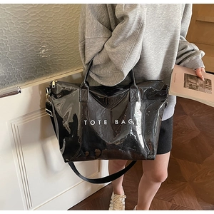 Detailed view of large black glossy tote bag with white TOTE BAG text and golden metal zipper
