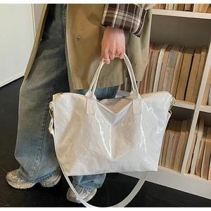 Detail of white glossy tote bag with embossed OTENBAG logo and dual carrying straps