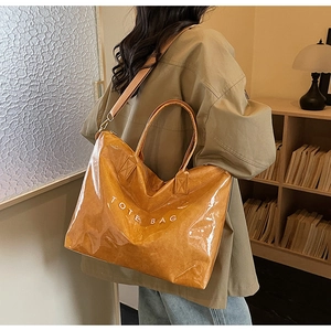 Detail of glossy yellow tote bag with white TOTE BAG lettering and wide shoulder strap