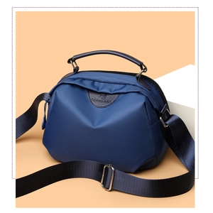 Detailed view of deep blue nylon bag with leather logo patch and wide shoulder strap