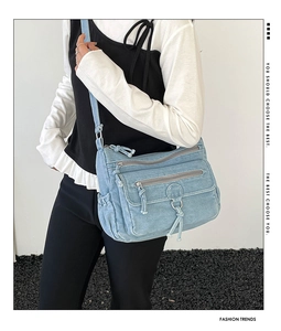 Detail view of denim crossbody bag featuring multiple zipper pockets and washed texture