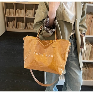 Detail of a shiny ginger yellow tote bag featuring adjustable strap and white text