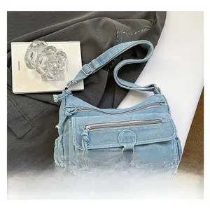 Detail of light blue denim crossbody bag featuring multiple zippers and fringe accents
