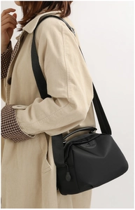 Side view of black oxford nylon crossbody bag with embossed logo on a casual beige outfit