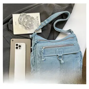 Detail of light blue denim crossbody bag featuring multiple zipper pockets and metal ring