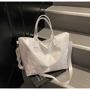 Detail of white wrinkled Tyvek tote bag featuring embossed TOTE BAG text and gold hardware