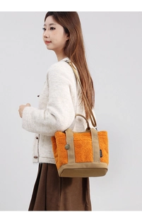Borsa tote in pile arancione con manici in tela kaki e tracolla presentata in uno studio
