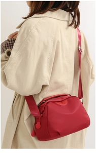 Detail of red oxford nylon shoulder bag with adjustable strap and logo pendant on beige coat