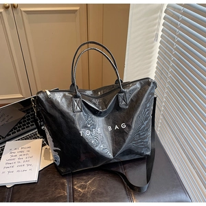 Detail of glossy black DuPont paper tote bag with white lettering on a leather chair
