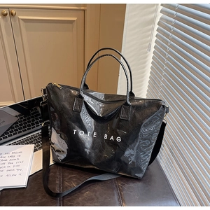 Detail view of a black glossy tote bag with white TOTE BAG text and a long shoulder strap