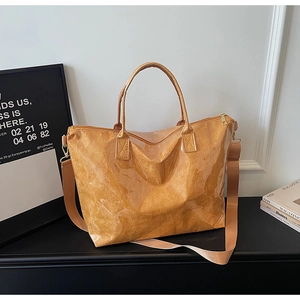 Detail of the high-gloss brown tote bag showing textured surface and wide nylon strap