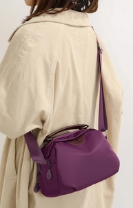 Detail of purple nylon crossbody bag with brown leather handles worn by a model