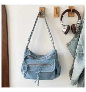 Detail of blue denim crossbody bag with multiple zippers and decorative metal ring