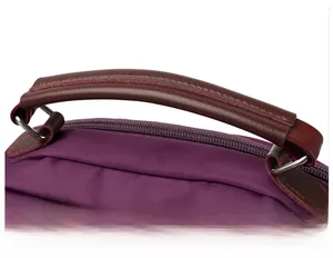 Detail of purple nylon handbag featuring brown faux leather handles and precision stitching