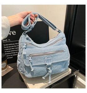 Detail of light blue denim crossbody bag featuring multiple zipper pockets and metal ring