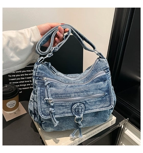 Detail view of denim shoulder bag with multi-zipper pockets and distressed edges