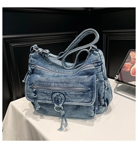 Detail of blue denim crossbody bag featuring multiple metal zippers and washed texture