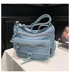 Detail of light blue denim shoulder bag showing zipper pockets and adjustable strap texture