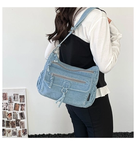 Detail of light blue denim crossbody bag featuring multiple zippers and adjustable strap